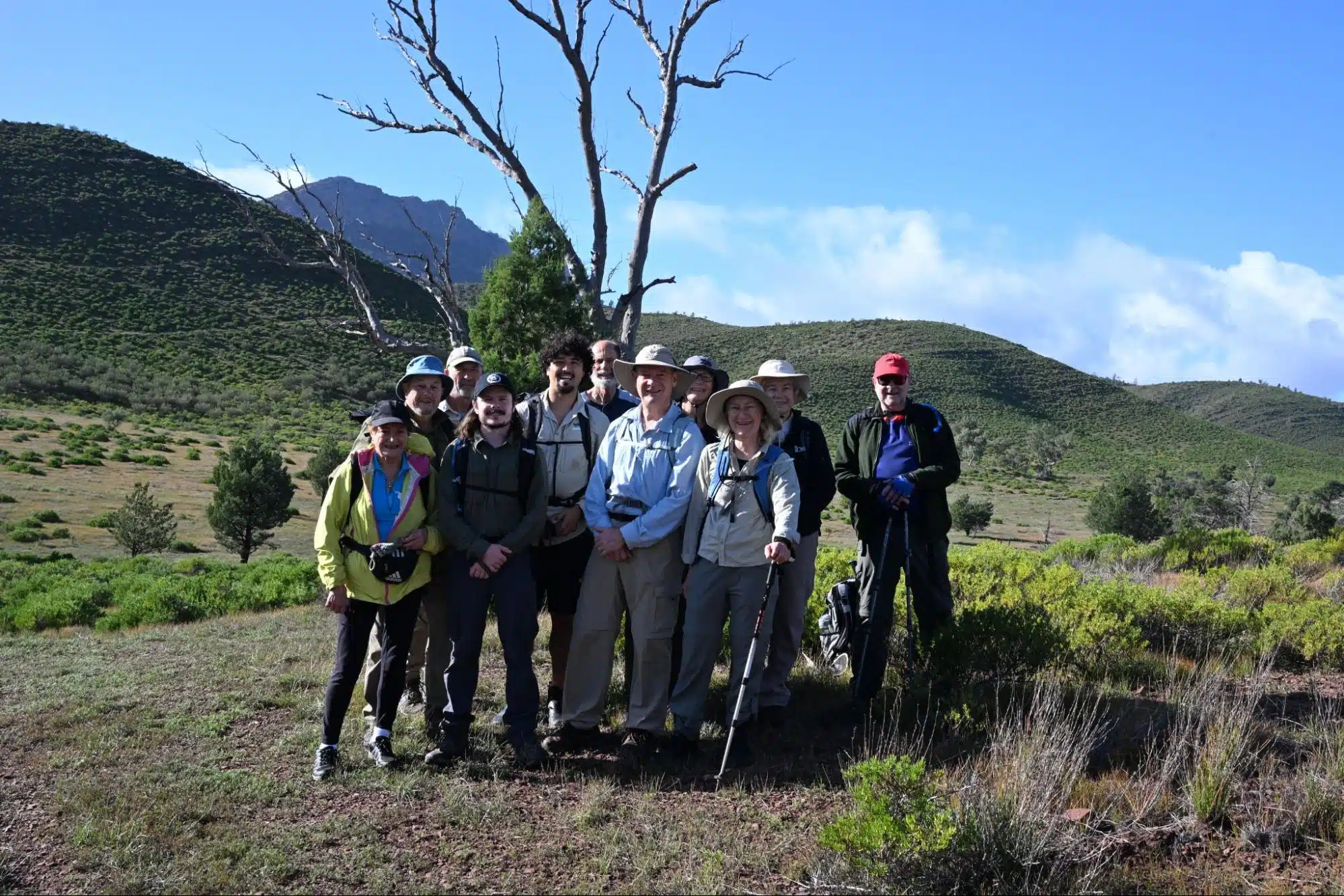 How fit do you need to be for an outback walking tour | Park Trek Group of hikers posing in a dry, hilly landscape with a bare tree and distant mountains under a blue sky.